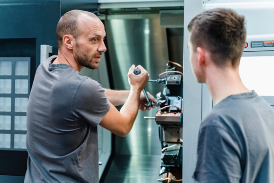 Expertise teaching trainee to tighten bolts of machine while standing at industry