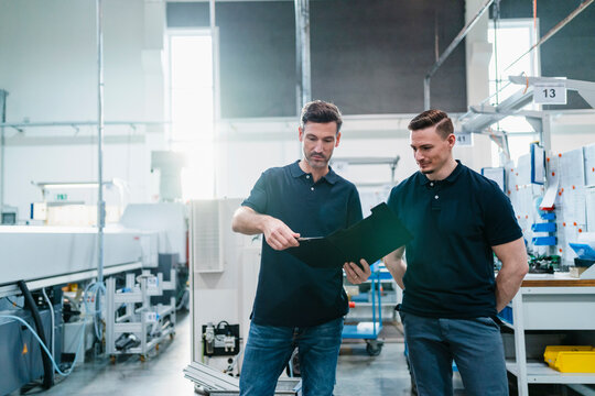 Male engineer with coworker reading file document in industry