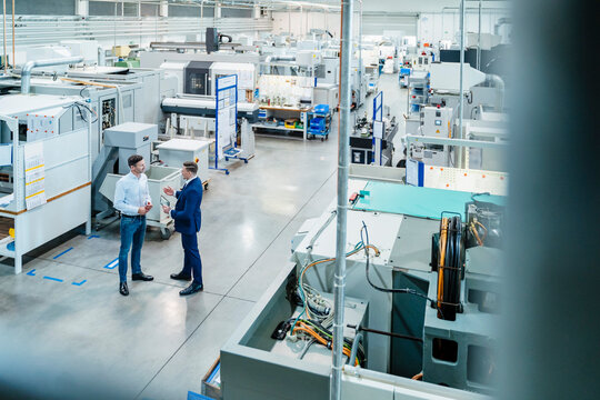 Businessman with male colleague discussing over digital tablet by machinery equipment