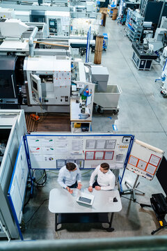 Businessman with male colleague discussing strategy on desk in factory