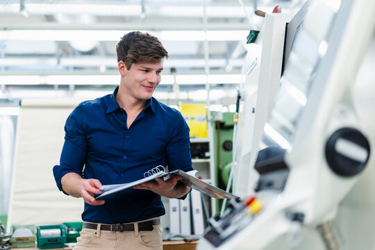 Smiling male engineer holding file document while examining manufacturing equipment in factory