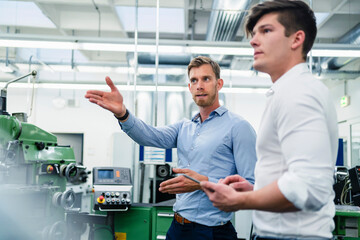 Businessman explaining male coworker about machinery in factory