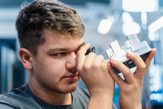 Young engineer examining small microscope while working at industry
