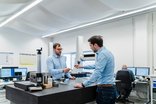 Engineers discussing over equipment while standing with coworker in background at office