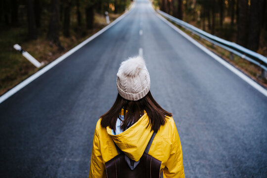 Woman in yellow raincoat standing on empty country road