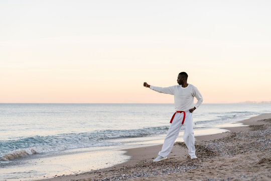 Adult man practicing martial arts on sandy coastal beach