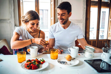 Happy young couple sitting at table and having breakfast at home