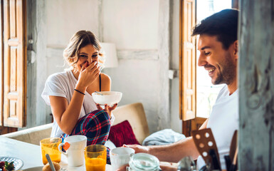 Happy young couple sitting at table and having breakfast at home