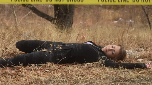 Body of female crime victim laying on grass pan reveals police tape - do not cross