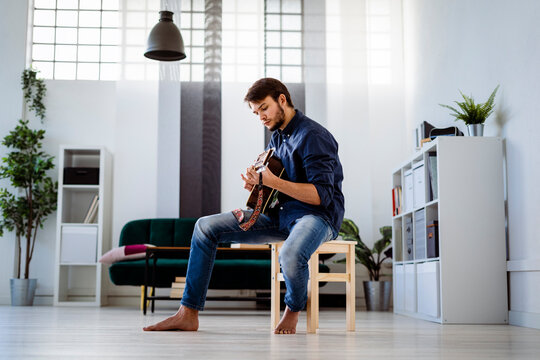 Professional doing rehearsal with guitar while sitting on stool at studio