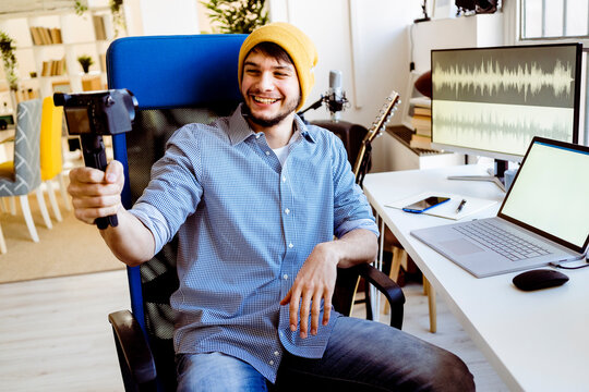 Musician with laptop smiling while recording on camera at studio