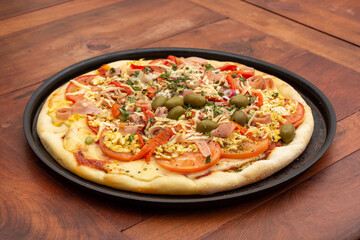 Delicious pizza with ham, cheese, tomato, egg and olives on wooden table.
