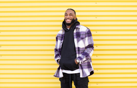 Happy young male rapper with hands in pockets against yellow corrugated wall