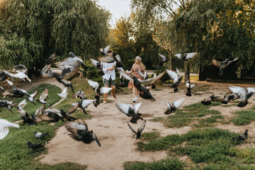 Lot of pigeons take off from ground in park while merry couple of man in love with woman approaching