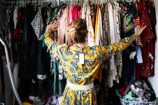 Fashionable blond woman in new yellow dress choosing from clothes rack at apartment