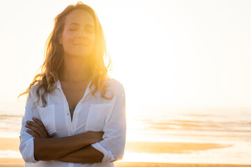 Woman standing with eyes crossed at beach during sunset