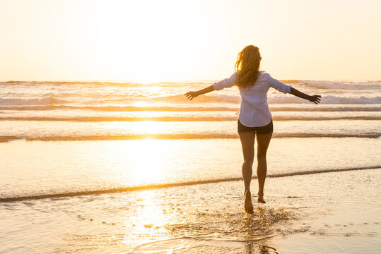 Carefree woman with arms outstretched running toward sea during sunset
