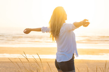 Woman standing with arms outstretched at beach during sunset
