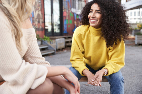 Smiling young woman talking with female friend while sitting on seat