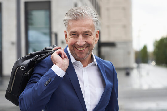 Smiling senior male entrepreneur holding laptop in city