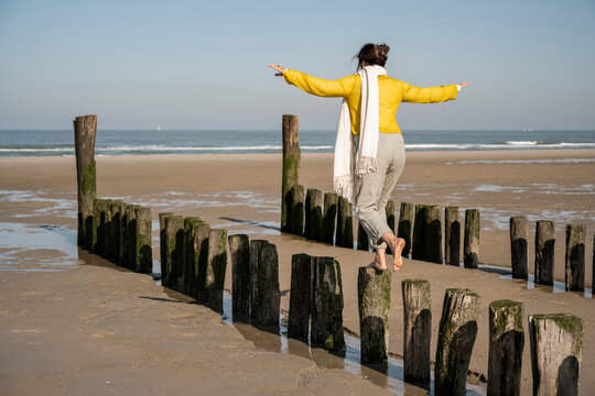 Mature woman with arms outstretched balancing on wooden posts at beach
