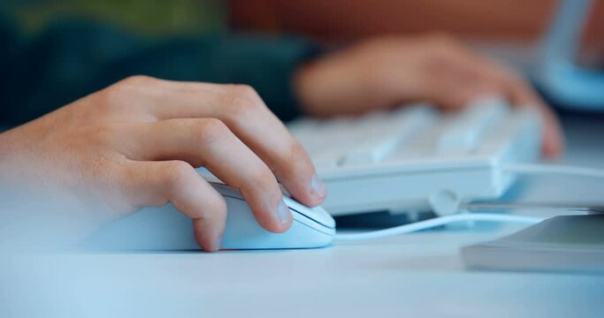 At a white table, a man works at a computer and moves a white wired mouse 