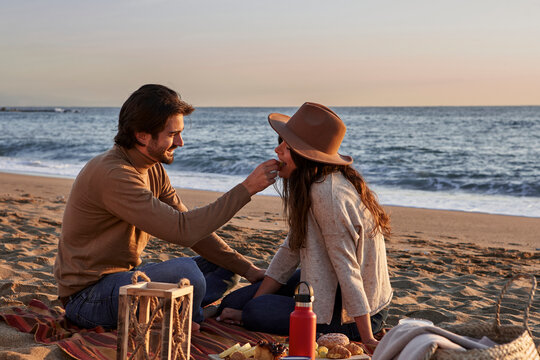 Smiling boyfriend feeding food to girlfriend while sitting on beach