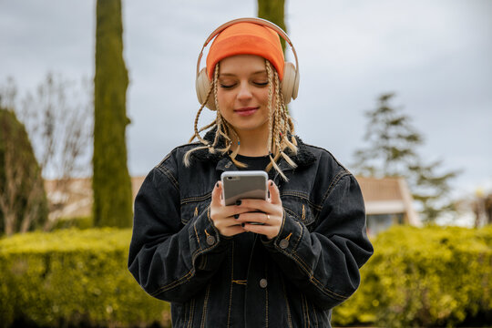 Fashionable woman in knit hat using smart phone while listening music