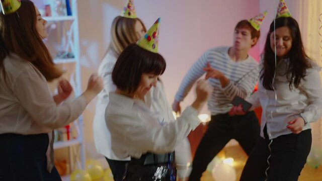 Relaxed group of friend dancing at birthday party as young woman sneezing and people running away. Scared Caucasian millennials celebrating on coronavirus pandemic.
