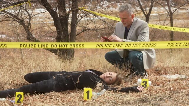 Detective takes pictures of deceased female victim at crime scene surrounded by police tape and evidence markers