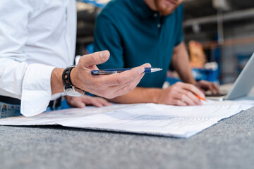 Hand of man holding pen while talking over documents with coworker