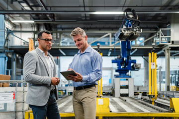 Mature manager working on digital tablet while businessman looking at it in industry