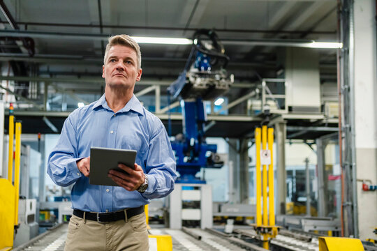 Mature supervisor holding digital tablet while looking away in industry