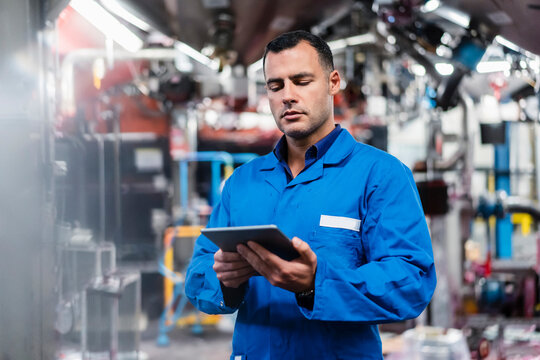 Engineer in blue coat working on digital tablet in factory