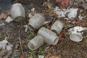 garbage from many dirty gray glass jars on the ground outside