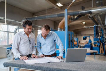 Two carpenters talking over documents in production hall