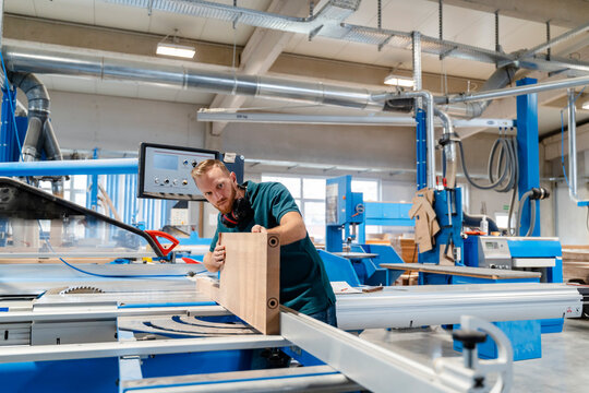 Carpenter measuring wooden plank in production hall