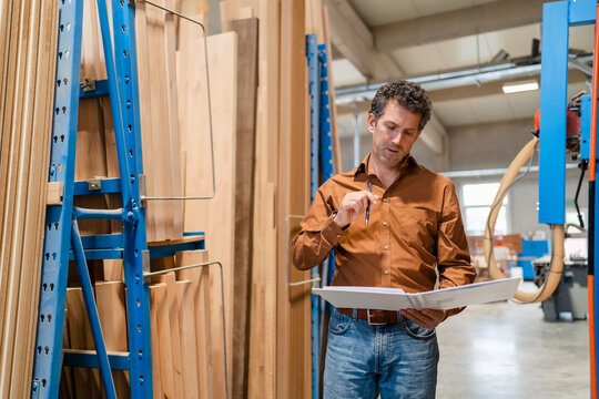 Portrait of carpenter standing with ring binder in front of shelves with wooden planks
