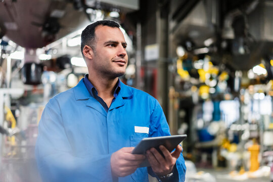 Smiling technician looking away while holding digital tablet in industry