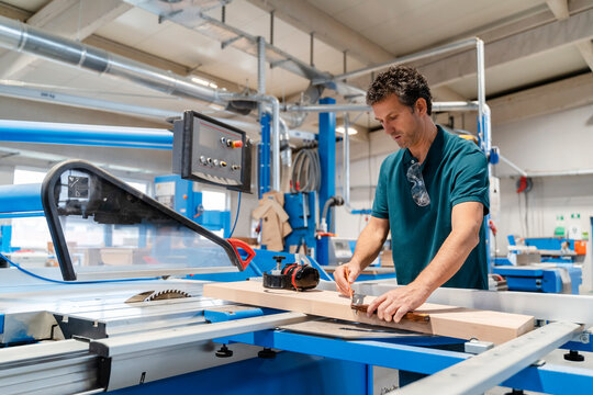 Carpenter measuring plank in front of circular saw
