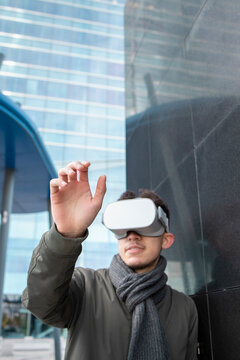Young man gesturing while watching on VR box by black wall