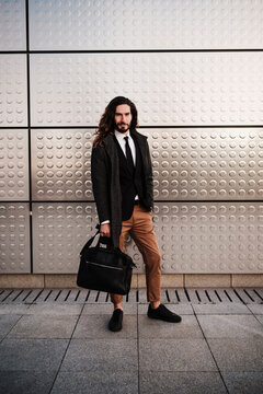 Entrepreneur wearing suit carrying briefcase while standing against silver wall