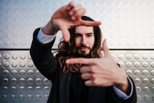 Businessman making finger frame while standing against silver wall