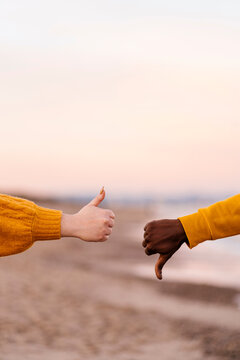 Couple showing thumps up and down gesture at beach