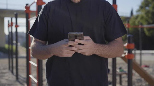 Close-up of hands using your smartphone, during outdoor calisthenics training. In the background is a bar park.