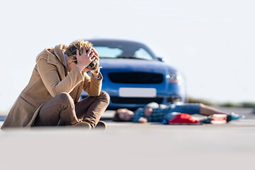 Desperate young man sitting on ground with boy in background lying by car after accident