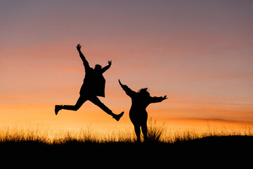 Carefree couple with arms outstretched standing against sky during sunset