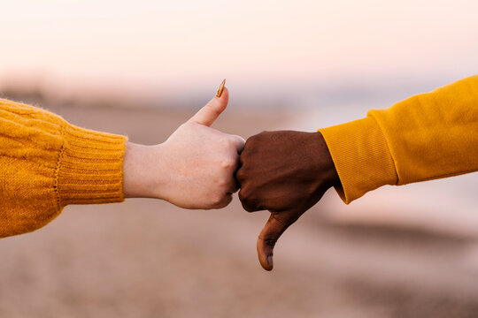 Man and woman gesturing with thumps up and down at beach