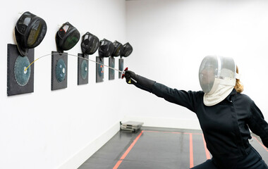 Woman hitting target with fencing sword at gym