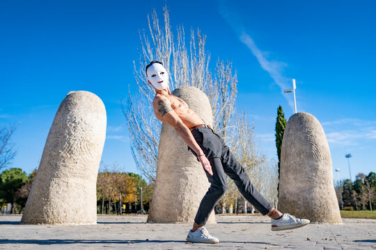 Shirtless man wearing white mask dancing while standing on footpath